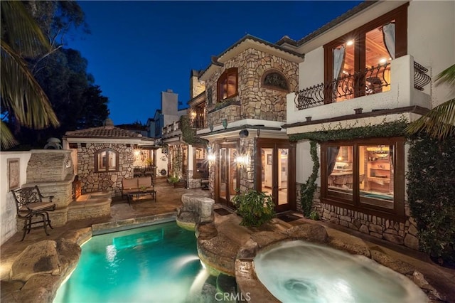 back house at twilight with a balcony, a swimming pool with hot tub, and a patio