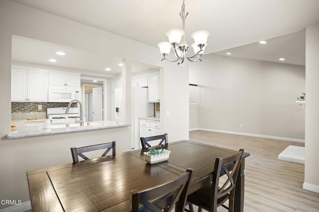 dining area with sink, an inviting chandelier, and light hardwood / wood-style flooring