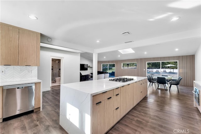 kitchen with light brown cabinetry, gas stovetop, stainless steel dishwasher, a kitchen island, and light stone countertops