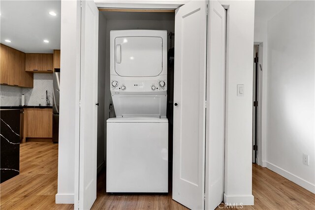 laundry area with light hardwood / wood-style flooring and stacked washer / dryer