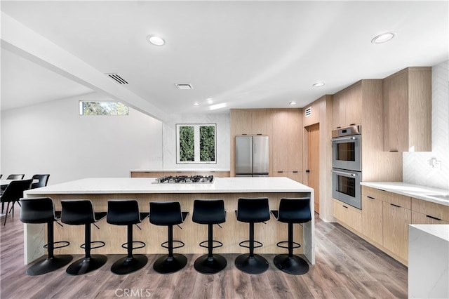 kitchen with vaulted ceiling, appliances with stainless steel finishes, a kitchen breakfast bar, a center island, and light wood-type flooring