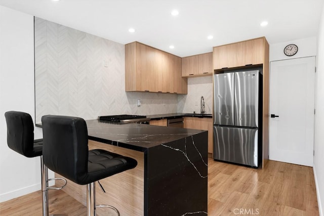 kitchen with sink, light hardwood / wood-style flooring, stainless steel fridge, a breakfast bar area, and kitchen peninsula