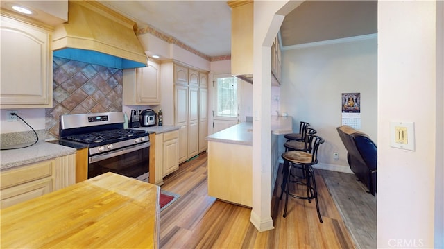 kitchen with crown molding, gas range, custom range hood, backsplash, and light hardwood / wood-style floors