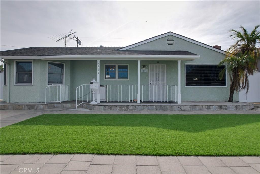 view of front of property featuring a front lawn, stucco siding, covered porch, and roof with shingles