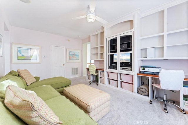 living room featuring ceiling fan, light colored carpet, and built in desk