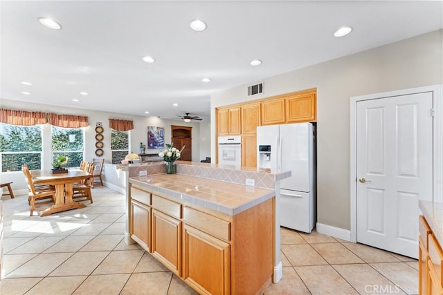 kitchen featuring ceiling fan, light tile patterned floors, white appliances, a kitchen island, and tile counters