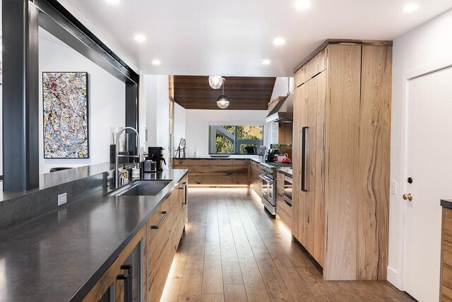 kitchen featuring light hardwood / wood-style flooring, light brown cabinetry, sink, wall chimney exhaust hood, and stainless steel stove