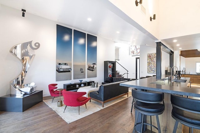 kitchen with dark countertops, a towering ceiling, a sink, a kitchen bar, and hardwood / wood-style flooring