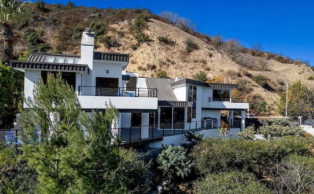 rear view of property with a standing seam roof, a chimney, metal roof, and stucco siding