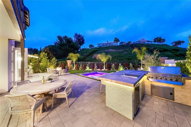 patio terrace at dusk with exterior kitchen, a grill, and a mountain view