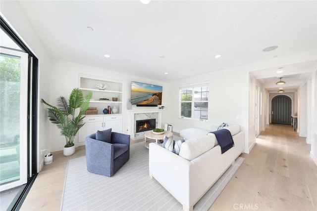 living room featuring built in features, light wood-type flooring, and a premium fireplace