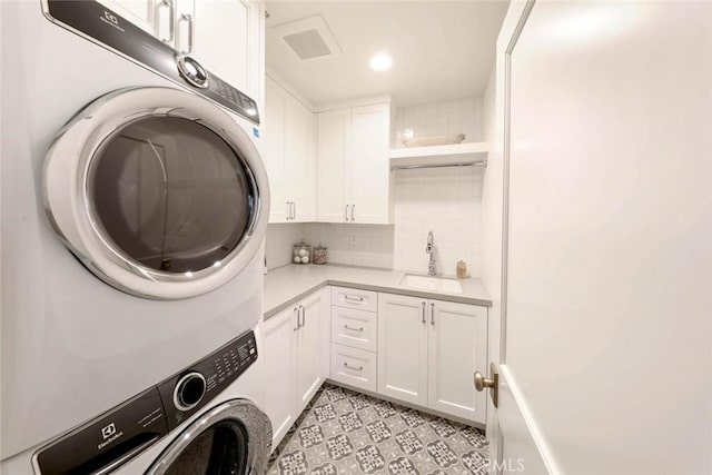 laundry room featuring sink, cabinets, stacked washer and clothes dryer, and light tile patterned floors