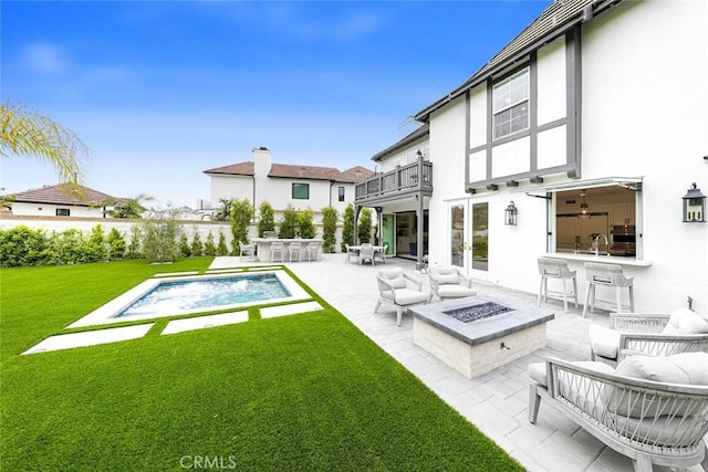 rear view of property with a balcony, exterior bar, an outdoor living space with a fire pit, a patio, and a yard