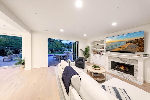 living room featuring built in features, light wood-type flooring, and a high end fireplace