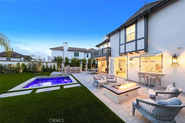 back house at dusk with a balcony, a lawn, an outdoor wet bar, a fenced in pool, and a patio area