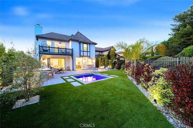 back of house with a balcony, a patio area, a fenced in pool, and a yard