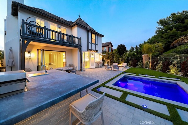 back house at dusk featuring a balcony, an outdoor fire pit, and a patio