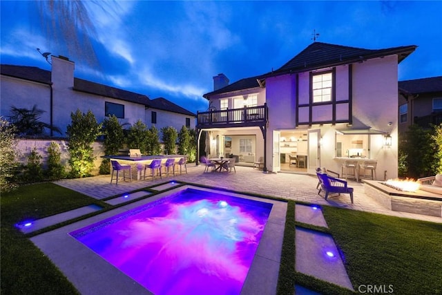 back of property featuring a balcony, a bar, a patio area, and a fire pit