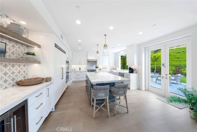 kitchen featuring wine cooler, hanging light fixtures, white cabinetry, tasteful backsplash, and a kitchen bar