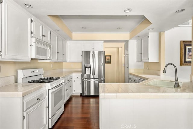 kitchen featuring kitchen peninsula, sink, white cabinets, a tray ceiling, and white appliances