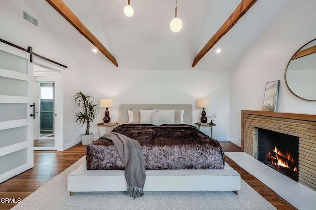 bedroom with dark wood-type flooring, lofted ceiling with beams, a barn door, and a fireplace