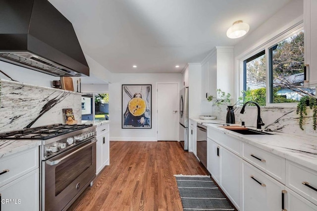 kitchen with backsplash, white cabinetry, light stone countertops, exhaust hood, and stainless steel appliances