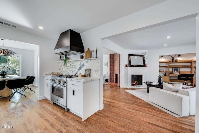 kitchen featuring exhaust hood, tasteful backsplash, white cabinetry, light wood-type flooring, and high end stainless steel range oven