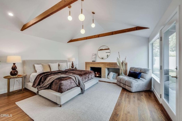 bedroom with hardwood / wood-style floors, lofted ceiling with beams, a brick fireplace, and access to outside