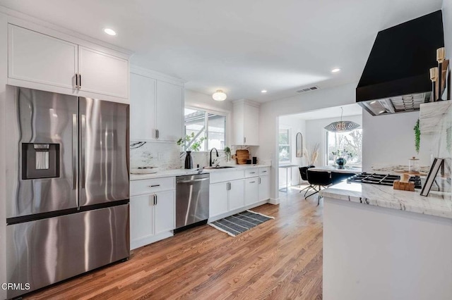 kitchen with light hardwood / wood-style floors, appliances with stainless steel finishes, white cabinetry, range hood, and pendant lighting