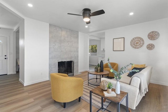 living room featuring light wood-type flooring, ceiling fan, and a tiled fireplace