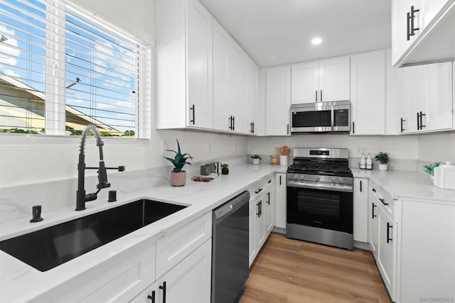 kitchen with light stone countertops, white cabinetry, sink, light hardwood / wood-style flooring, and stainless steel appliances