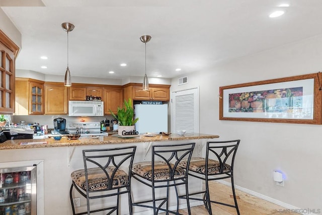 kitchen with white appliances, hanging light fixtures, kitchen peninsula, light stone counters, and beverage cooler