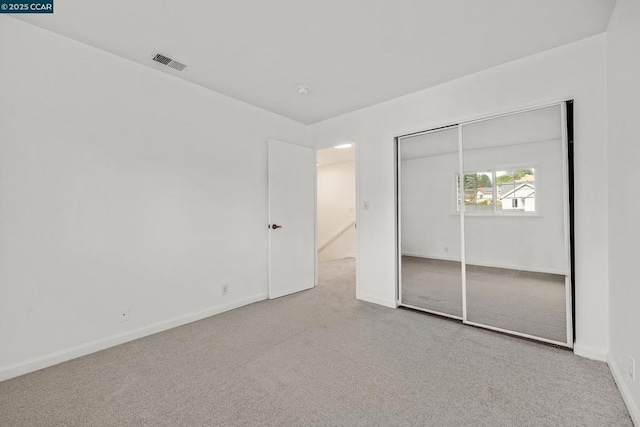 unfurnished bedroom with light colored carpet and a closet