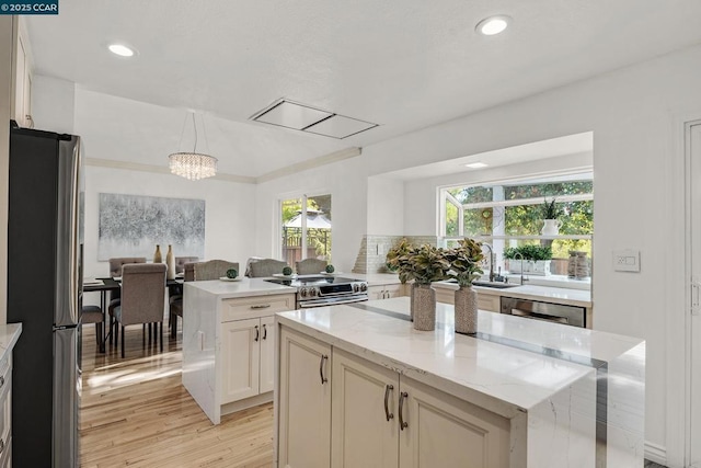 kitchen with pendant lighting, a wealth of natural light, light stone counters, a kitchen island, and stainless steel appliances