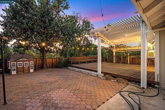 patio terrace at dusk with a deck, a pergola, and a storage unit