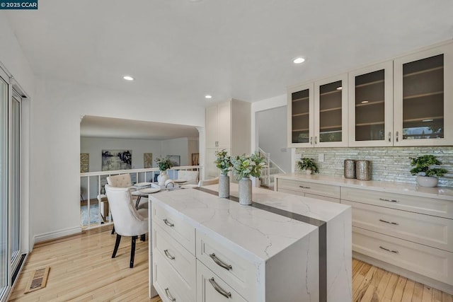 kitchen with backsplash, white cabinetry, light wood-type flooring, light stone countertops, and a center island