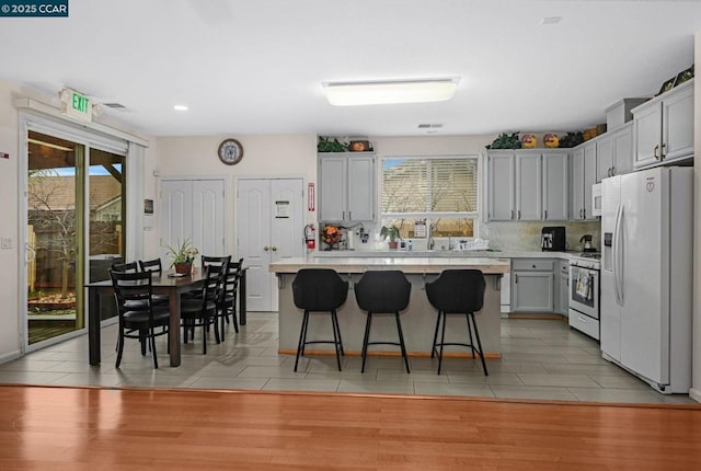 kitchen with a kitchen breakfast bar, white appliances, light tile patterned floors, and a kitchen island