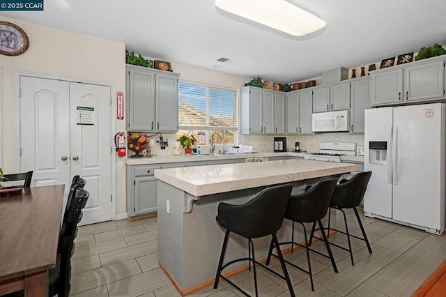 kitchen with sink, white appliances, a center island, a breakfast bar, and decorative backsplash