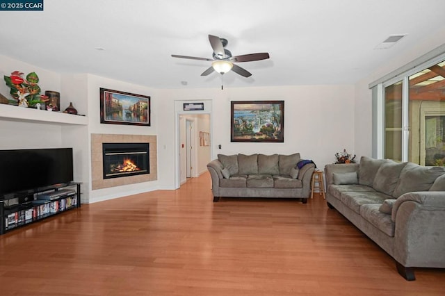 living room featuring ceiling fan, light hardwood / wood-style flooring, and a tiled fireplace