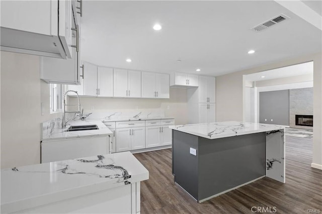 kitchen featuring sink, light stone countertops, a center island, and white cabinets