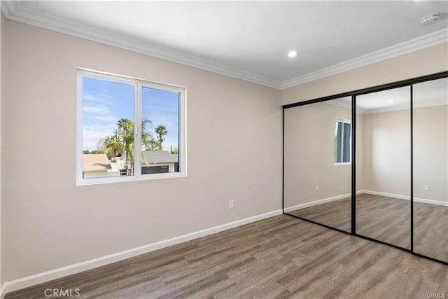 unfurnished bedroom featuring hardwood / wood-style flooring, ornamental molding, and a closet