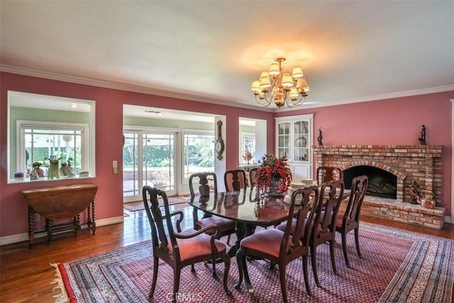 dining room featuring dark wood-type flooring, ornamental molding, a chandelier, and a fireplace