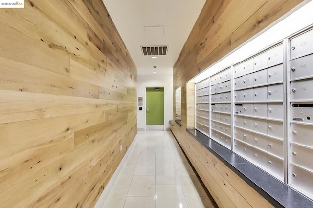 hall with tile patterned floors, wooden walls, and a mail area