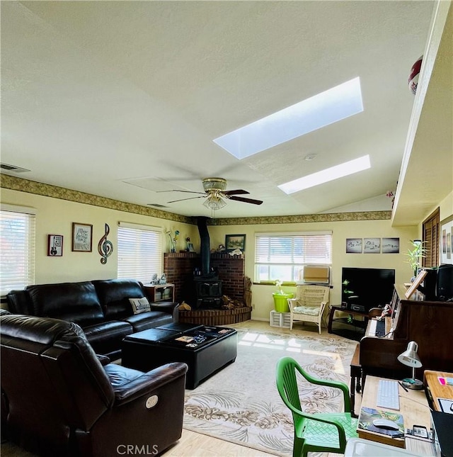 living room with ceiling fan, a wood stove, and lofted ceiling with skylight