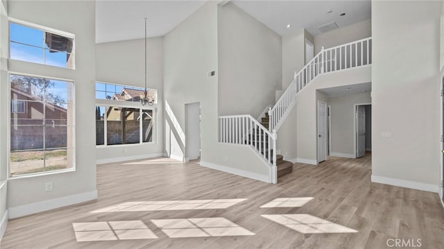 unfurnished living room featuring an inviting chandelier, stairs, baseboards, and wood finished floors