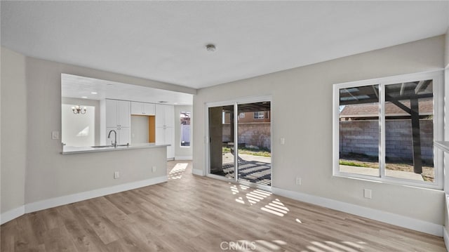 unfurnished living room with sink, a chandelier, and light wood-type flooring