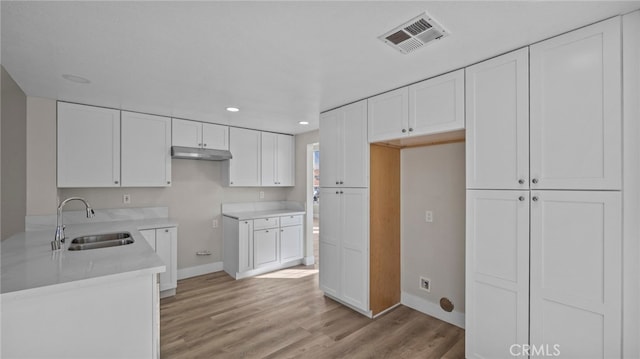 kitchen with visible vents, white cabinets, light countertops, light wood-style floors, and a sink