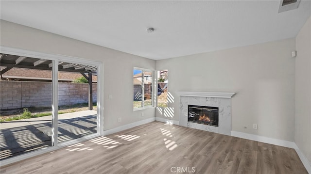 unfurnished living room with a high end fireplace, visible vents, baseboards, and wood finished floors