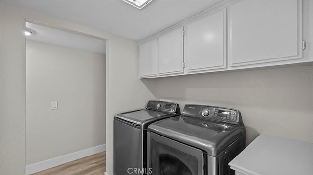 laundry room featuring cabinets, washing machine and clothes dryer, and light wood-type flooring