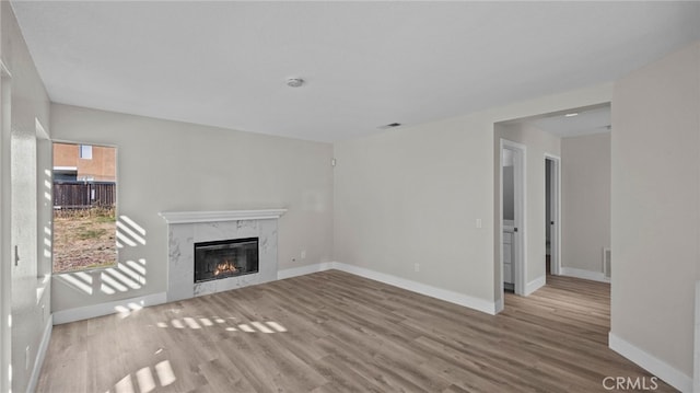 unfurnished living room with a high end fireplace and light wood-type flooring